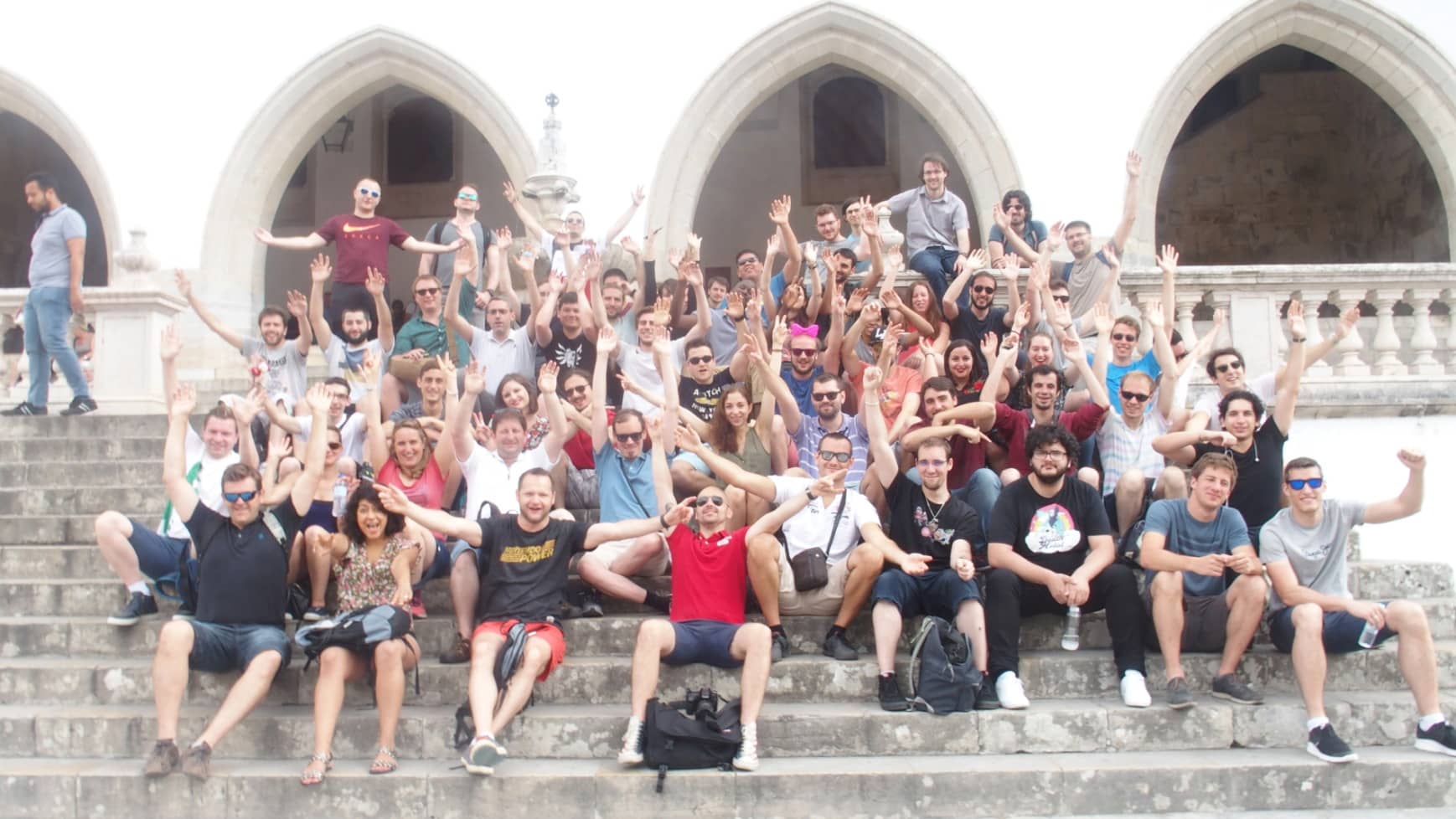 Photo de groupe Takima. L'ensemble des personnes sont assises sur des marches d'escaliers en levant les bras en l'air pour la photo