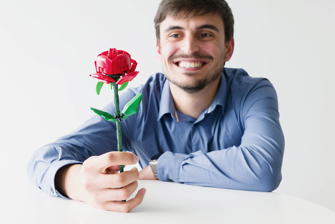 Homme souriant en train de regarder une fleur en Lego