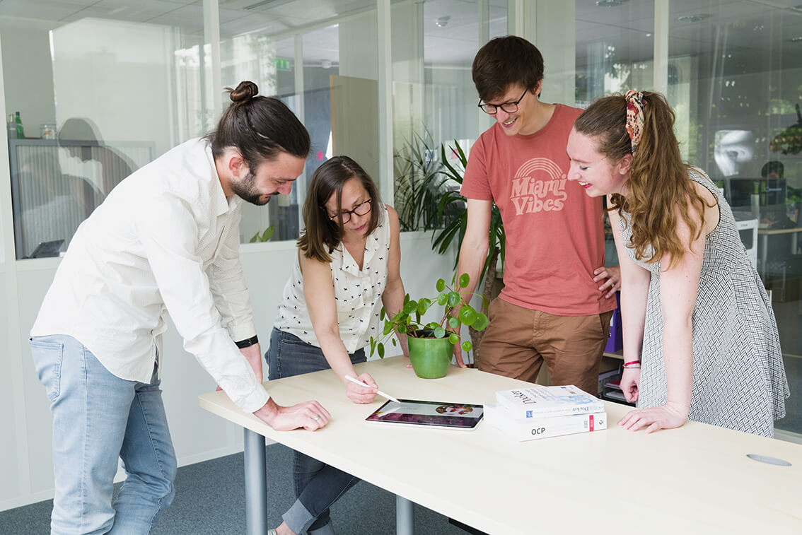Groupe de quatre collègues souriants regardant une tablette autour d’une table